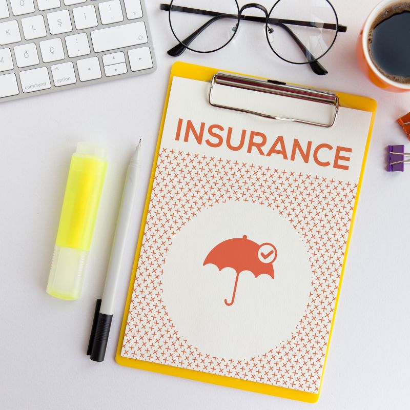 folder that says "Insurance" on a clip board by a keyboard, pen, glasses, and coffee cup