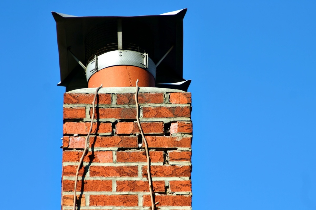 A chimney set against a blue sky with it's missing mortar very visible
