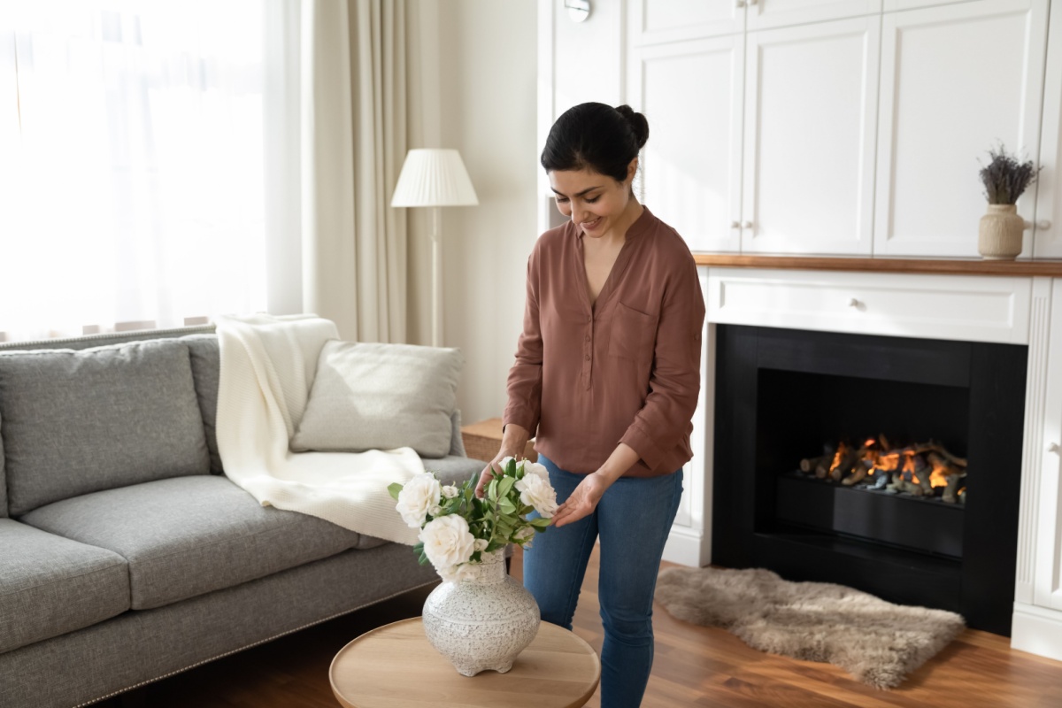 a woman arranging flowers on the coffee table with a fire crackling behind her